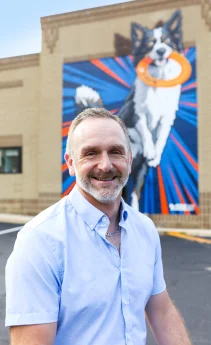 Dr. Steve Horvath standing outside the veterinary clinic beside his dog mural